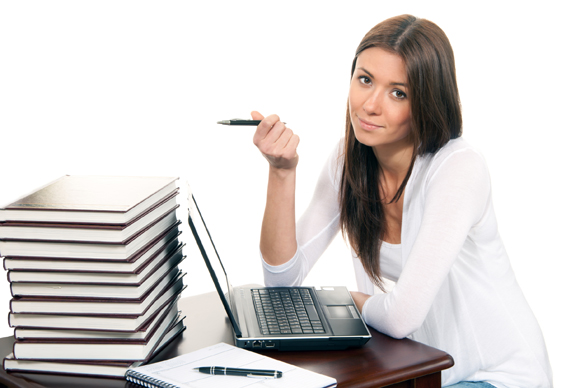 Brunette Business woman sitting in an office working on her laptop computer pc with a pen in the hand offer to sign contract, on the table books, paper and notebook isolated on a white background
